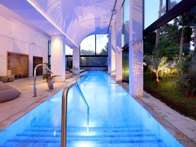 Indoor swimming pool with blue water and garden view, surrounded by lounge chairs and soft lighting.