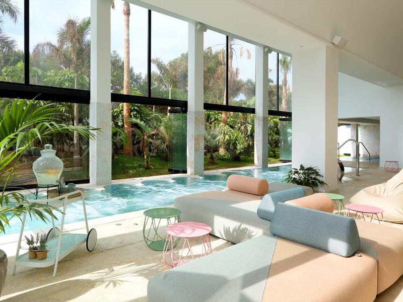 Modern indoor pool area with large windows, colorful seating, and lush outdoor garden view.