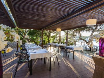 Terasa restaurace s prostřenými stoly pod dřevěnou pergolou, obklopená stromy.