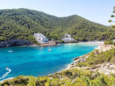 Tyrkysový záliv obklopený zelenými kopci s bílými budovami u vody.