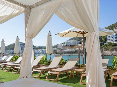 Lehátka pod baldachýnem s výhledem na bazén a moře, jasná obloha.