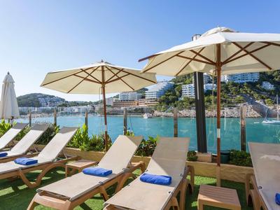 Sonnige Strandpromenade mit Liegestühlen, großen Sonnenschirmen und blauem Meer im Hintergrund.