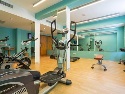 Moderner Fitnessraum mit verschiedenen Trainingsgeräten und großen Spiegeln an den Wänden.