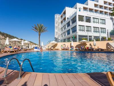 Modrý bazén s lehátky a moderním hotelem pod jasnou oblohou.