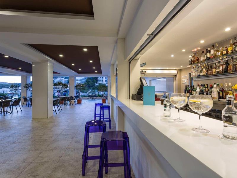 Moderní bar s fialovými stoličkami a výhledem na venkovní terasu s stolky.