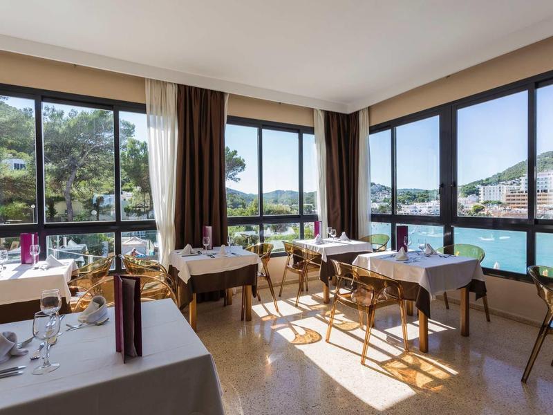 Světla místnost s velkými okny a výhledem na moře, elegantní stoly a židle.