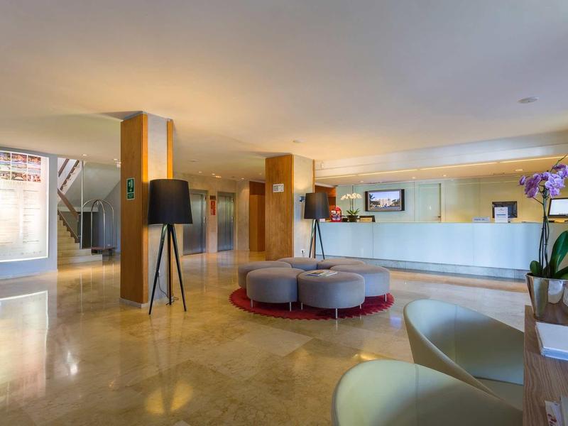 Světlá hotelová hala s moderním nábytkem a bílou recepcí.