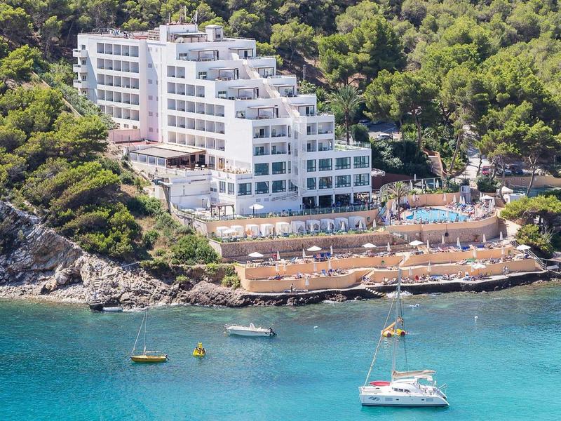 Moderní terasový hotel u tyrkysové vody s loděmi a hustým lesem.