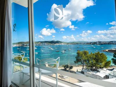 Uitzicht vanaf een balkon met witte stoelen op een strand en zee onder een blauwe lucht.