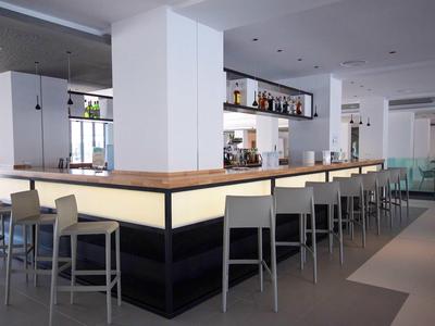 Moderne hotelbar met verlichte toonbank en grijze barkrukken in een lichte omgeving.