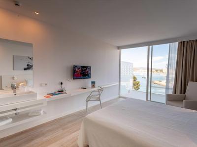 Modern hotelkamer met tweepersoonsbed, bureau, tv en groot raam met uitzicht op zee.