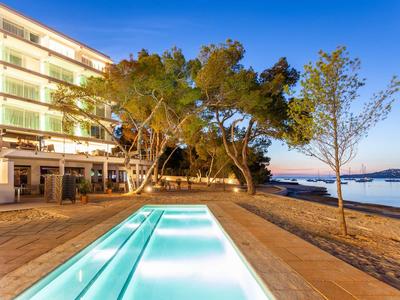 Piscina moderna con acqua illuminata accanto a hotel sulla spiaggia al tramonto.