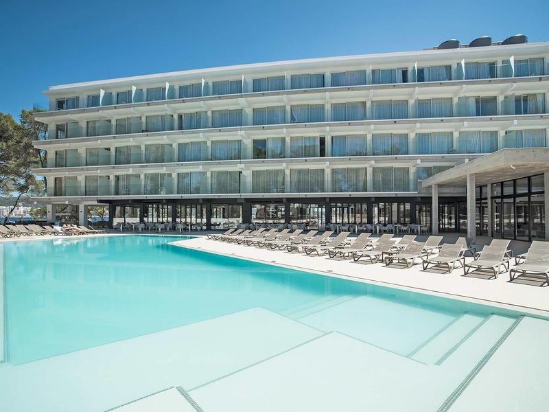 Modern hotelcomplex met groot buitenzwembad en ligstoelen bij zonnig weer.