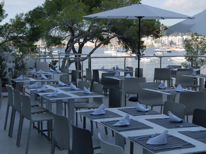 Buitenplaatsen met tafels, stoelen en parasols met uitzicht op water en stadsgezicht.
