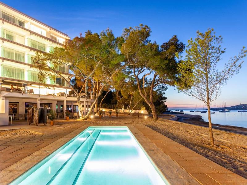 Verwarmd zwembad met hotelgebouw en strand bij zonsondergang.