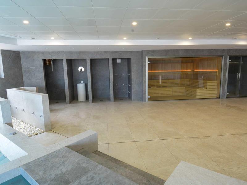 Grote lege binnenruimte met grijze tegels en glazen wand naast meerdere deuren.