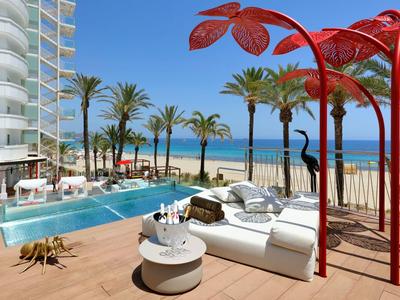 Hotelová terasa s bazénem, výhledem na pláž a červenými slunečníky v tropickém prostředí