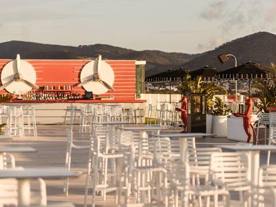 Terasa s bílými židlemi a stoly, větrné turbíny a hory v pozadí při západu slunce.