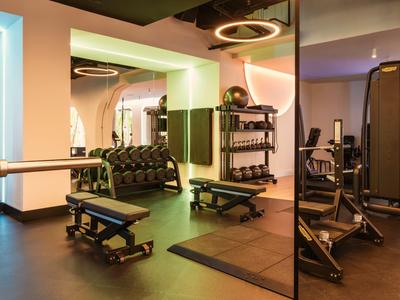 Moderner Fitnessraum mit Hanteln, Bänken und Spiegelflächen in warmem Licht.