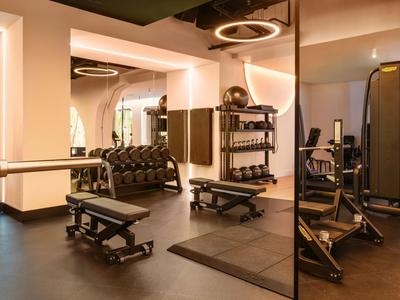 Moderner Fitnessraum mit Hanteln, Bänken und Spiegeln in einem Hotel.