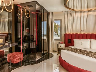Elegantes Hotelzimmer mit rundem Bett, rotem Polster und moderner Einrichtung mit Blick auf das Meer.