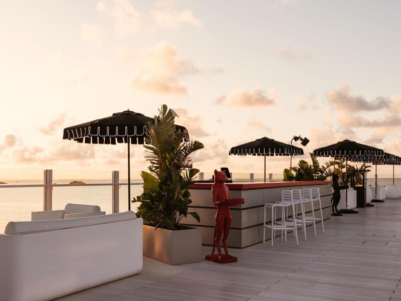 Elegantní střešní terasa s barem, bílým posezením a dekorativními rostlinami při západu slunce