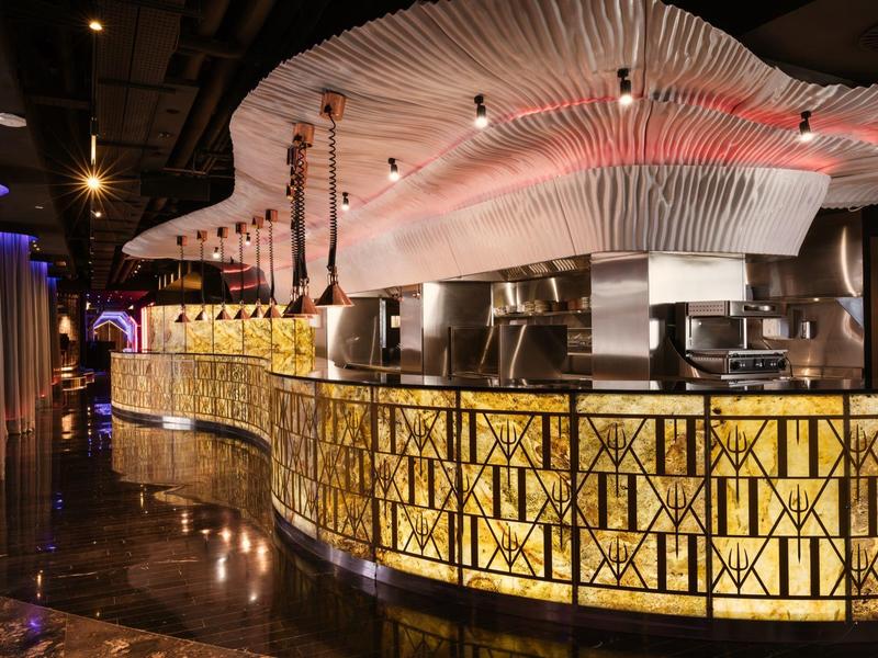 Luxusní hotelový bar se zakřiveným osvětleným pultem a moderním designem.