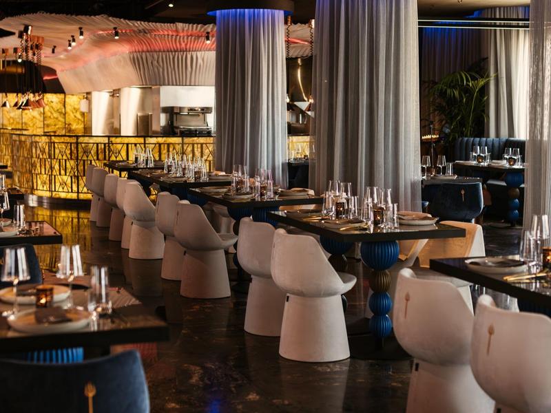 Elegantní restaurace s prostřenými stoly a moderními bílými židlemi ve stlumeném osvětlení.