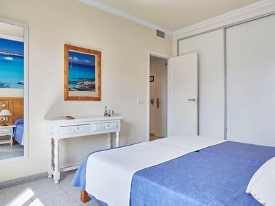 Chambre d'hôtel lumineuse avec lit double, bureau blanc, miroir et photos de plage au mur.