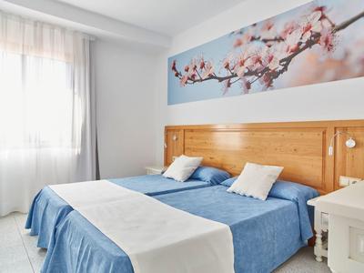 Chambre lumineuse avec deux lits simples, couvertures bleues et une décoration murale de fleurs de cerisier.