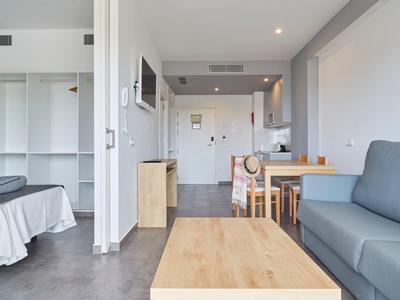 Chambre d'hôtel moderne avec coin salon, table à manger, placard ouvert et lit.