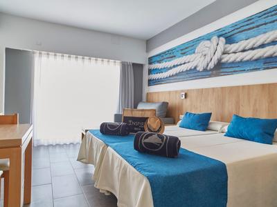 Chambre d'hôtel moderne avec deux lits, décoration bleue et blanche, et lumière naturelle.