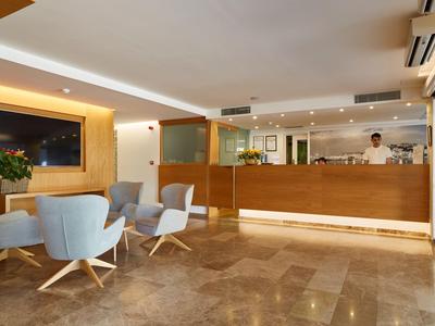 Nowoczesna lobby hotelowa z recepcją i miejscem do siedzenia, jasne kolory i ciepłe oświetlenie.