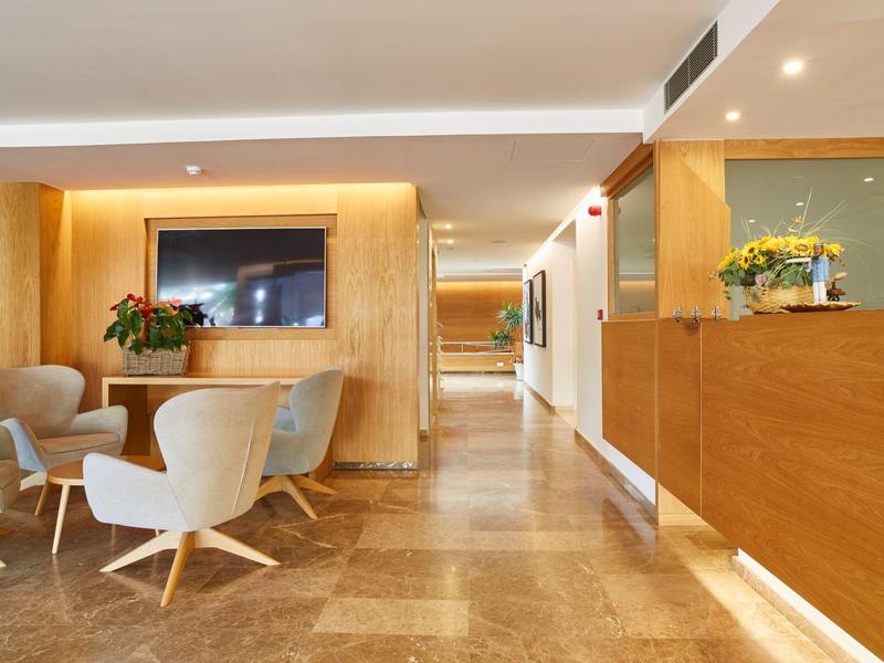 Hall d'hôtel lumineux avec fauteuils confortables, mur en bois et sol carrelé clair.