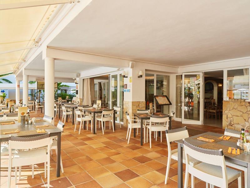 Terrasse extérieure couverte d'un hôtel avec plusieurs tables et chaises en plein jour.
