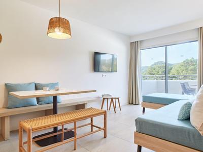 Světlý obývací pokoj s moderní lavicí, televizí a přístupem na balkon s výhledem na zelenou krajinu.