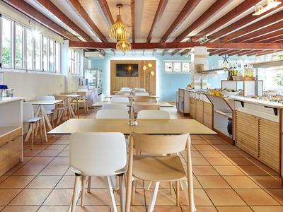 Světlá moderní kavárna s dřevěnými trámky na stropě, bílými židlemi a velkou bufetovou částí.