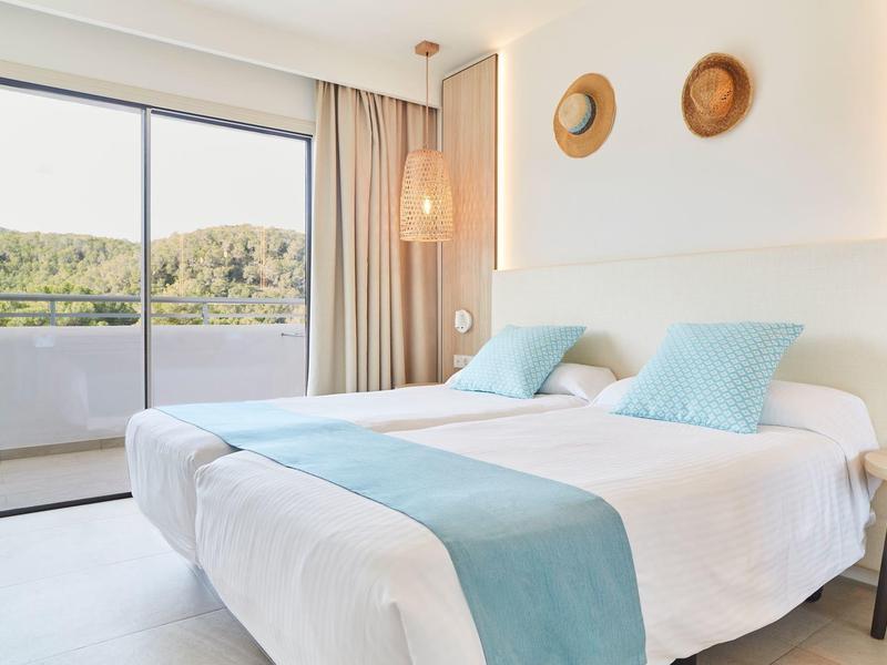 Světý hotelový pokoj se dvěma jednolůžky a výhledem na zelenou krajinu přes velká okna.