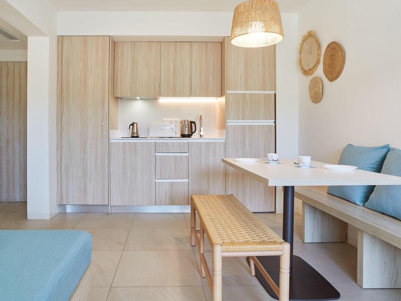 Moderní kuchyňský prostor se dřevěným nábytkem, jídelní lavice a modré polštáře v jasné místnosti.