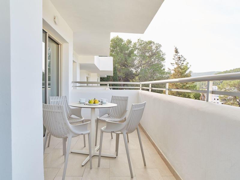 Balkon s kulatým stolem, čtyřmi židlemi a talířem citrusů, obklopený bílým zábradlím.