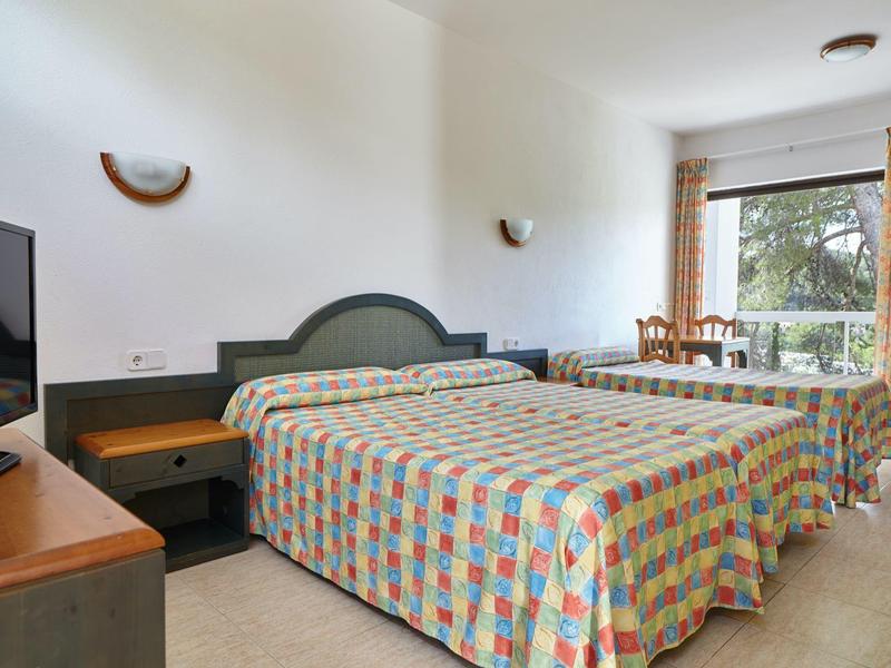 Hotelový pokoj se dvěma postelemi, barevnými přikrývkami, psacím stolem a oknem se závěsy