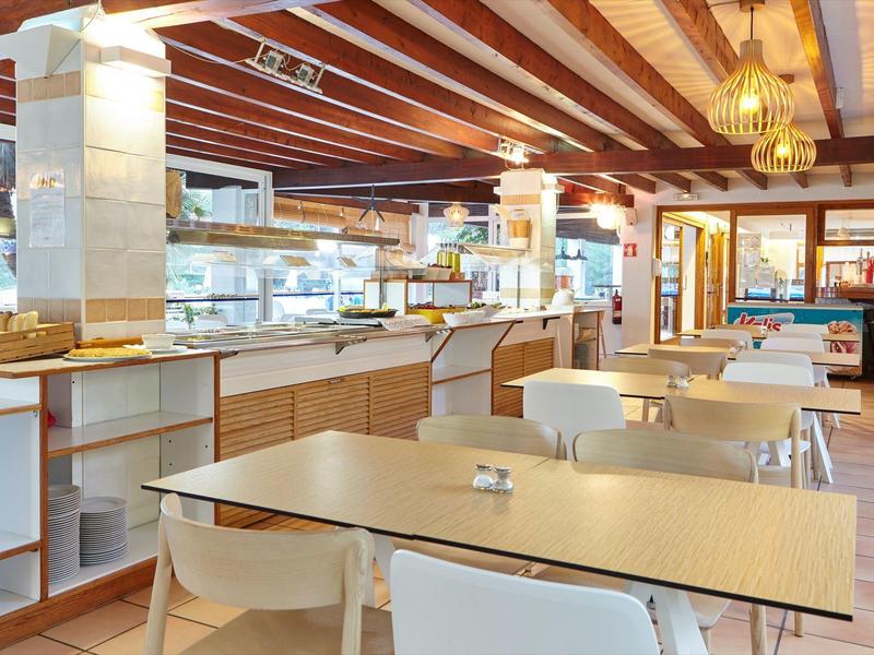 Světlá snídaňová místnost se stoly, židlemi a bufetovou částí pod dřevěným stropem.