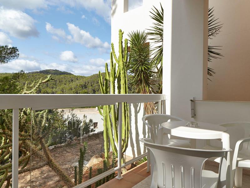 Balkon s bílým stolem a židlemi s výhledem na zelené kopce a kaktusovou zahradu.