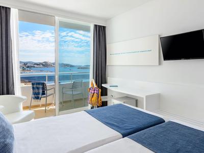 Habitación de hotel moderna con dos camas, televisor y balcón con vistas al mar.