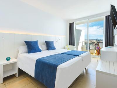 Habitación de hotel luminosa con cama doble, ropa de cama azul y balcón con vista al mar.