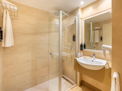 Baño moderno con ducha, lavabo, espejo y toallas en tonos beige cálidos.