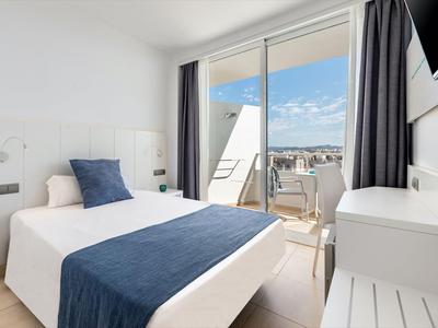 Habitación de hotel luminosa con cama, balcón y vista a la ciudad.