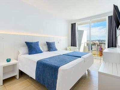 Habitación de hotel moderna con cama doble, colcha azul y vista al balcón y al mar.