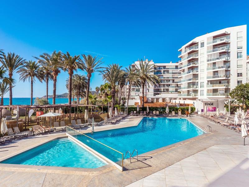 Moderner Hotelpool mit Sonnenterrasse, Palmen und Blick auf das Meer unter klarem Himmel.