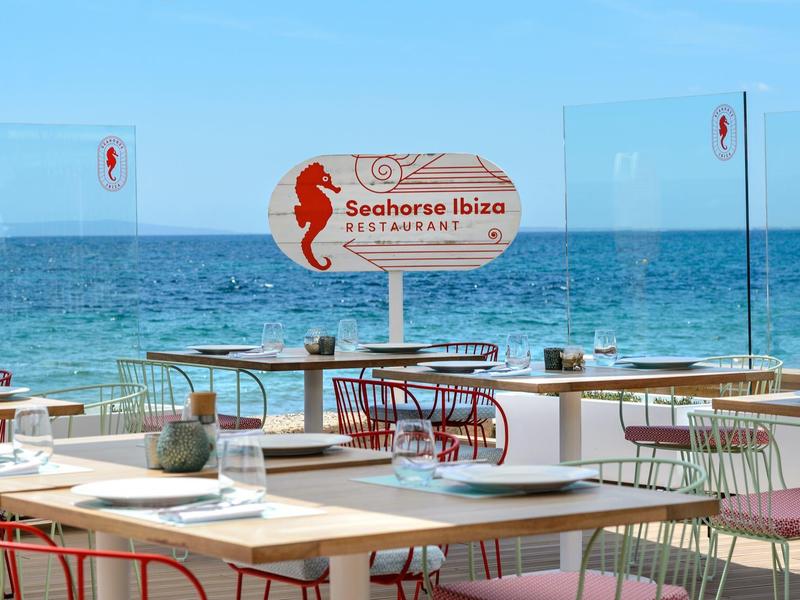 Restaurant mit Tischen und Stühlen direkt am Strand mit Blick auf das blaue Meer.